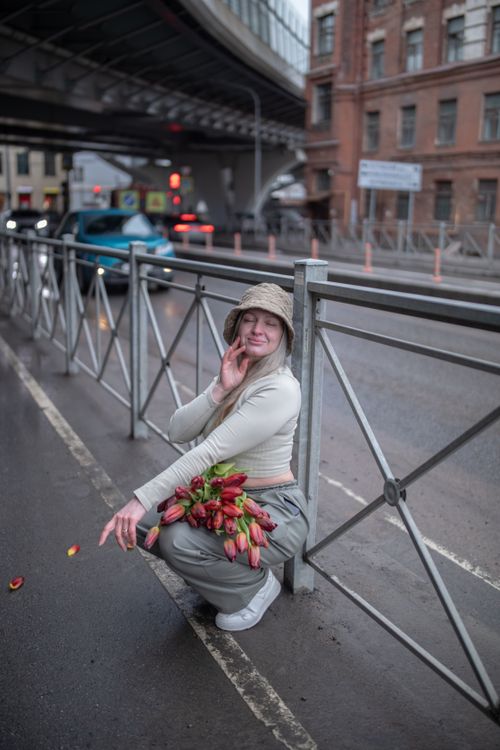Free A woman in a hat poses with tulips on a rainy urban street, capturing a candid city moment. Stock Photo