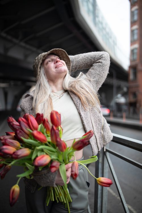 Free Joyful woman with tulips posing stylishly on an urban street, capturing spring vibes. Stock Photo