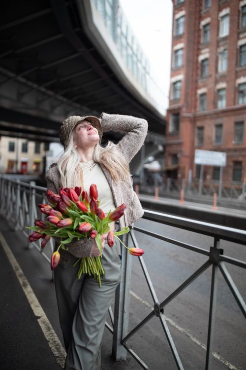 Free Elegant woman with blonde hair holding a tulip bouquet under a city bridge. Stock Photo