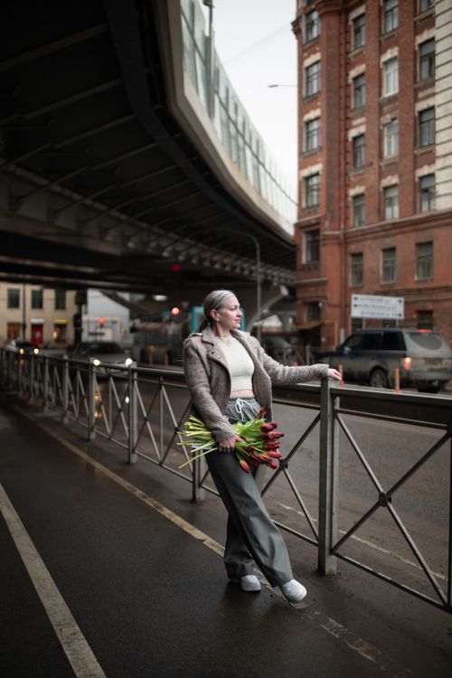 Free Woman holding tulips by an urban street railing, wearing a jacket. Stock Photo