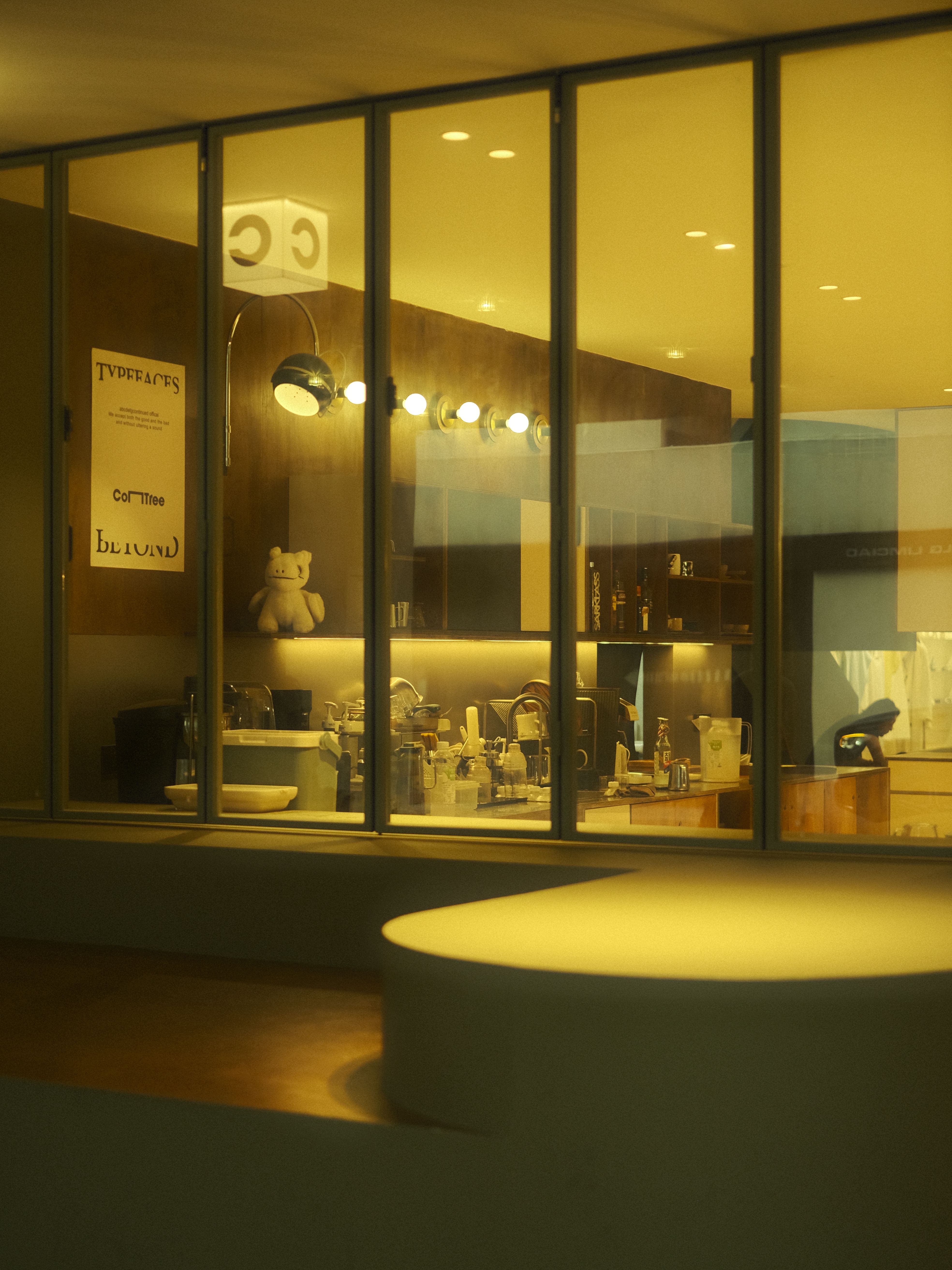 Warmly lit modern kitchen interior captured through glass windows with a cozy ambiance.