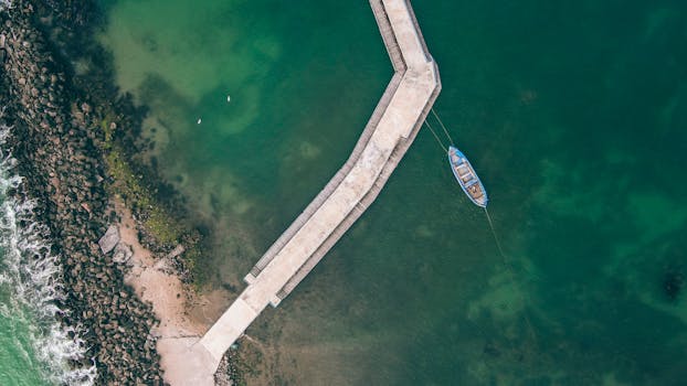 Scenic aerial view of a pier and boat along the coast in Nessebar, Bulgaria. Crystal clear waters and shoreline are visible.