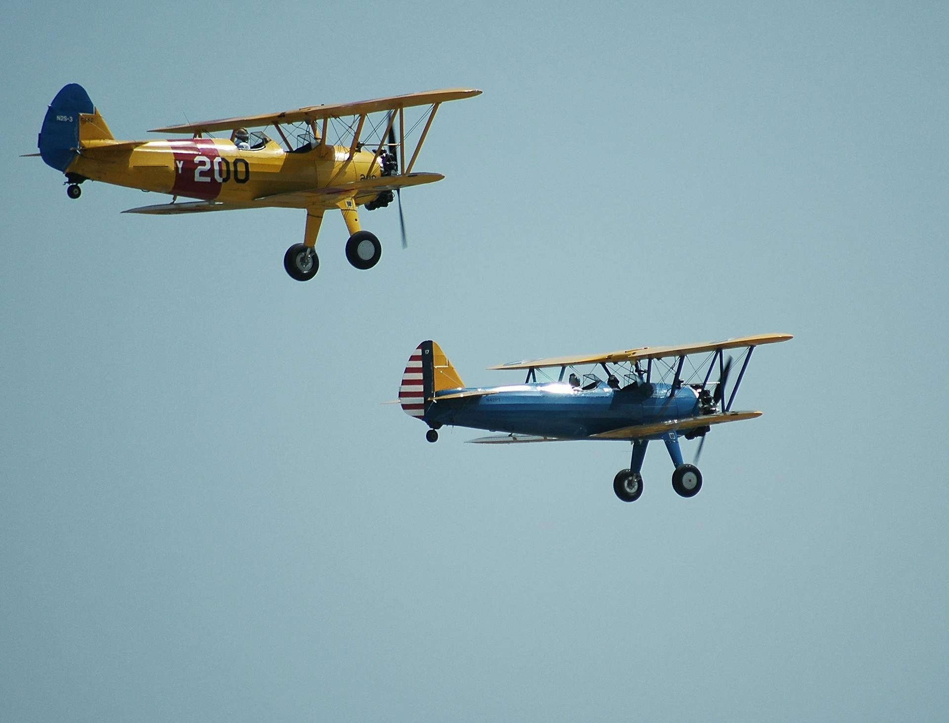 Two classic biplanes soaring side by side in a clear blue sky, showcasing aviation history.