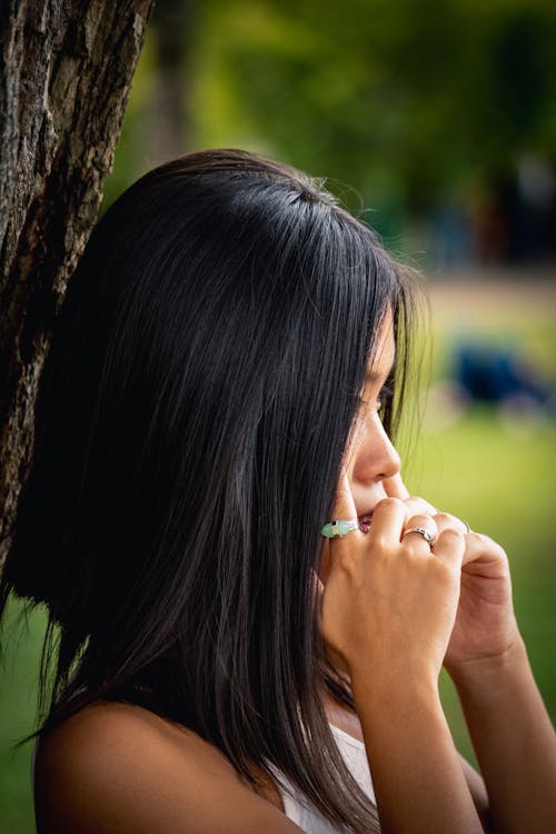 Side View Photo of Woman Standing by a Tree Holding Her Temple