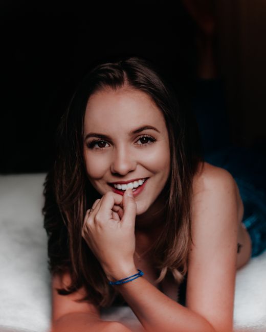 Portrait of a smiling woman lying on a bed, conveying natural beauty and elegance indoors.