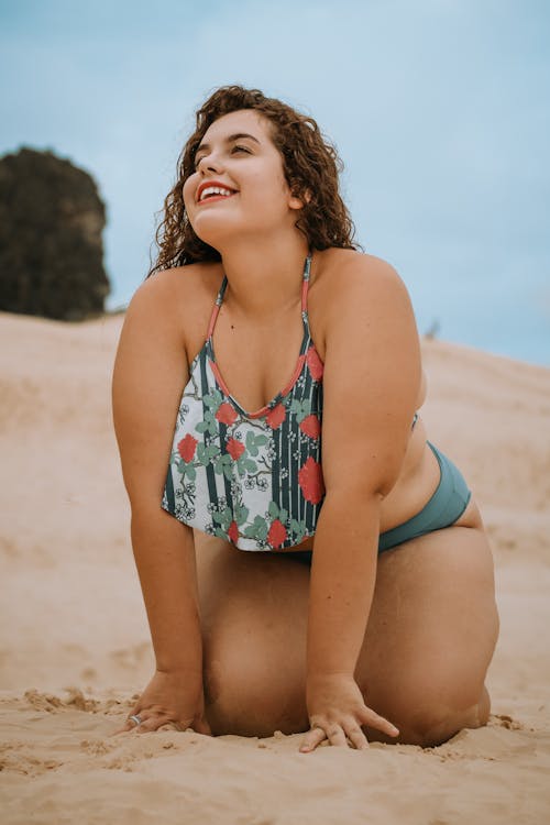 跪在棕色沙灘上，一邊微笑的女人