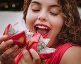 特写镜头中，一位微笑的女人即将品尝多汁的火龙果，鲜艳的色彩展露无遗