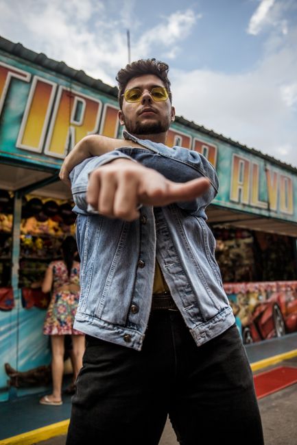 A stylish man in a denim jacket and sunglasses posing confidently at a São Paulo amusement park.