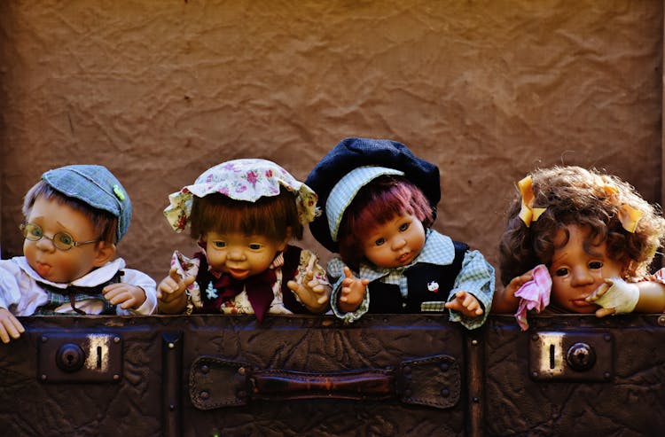 Four Dolls Near Brown Leather Bags