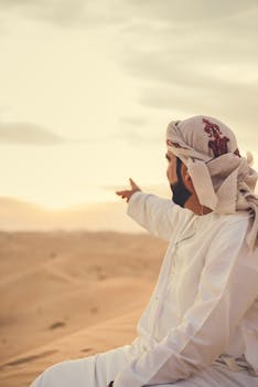 日落时分，一名戴着头巾的男子指着迪拜风景优美的沙漠