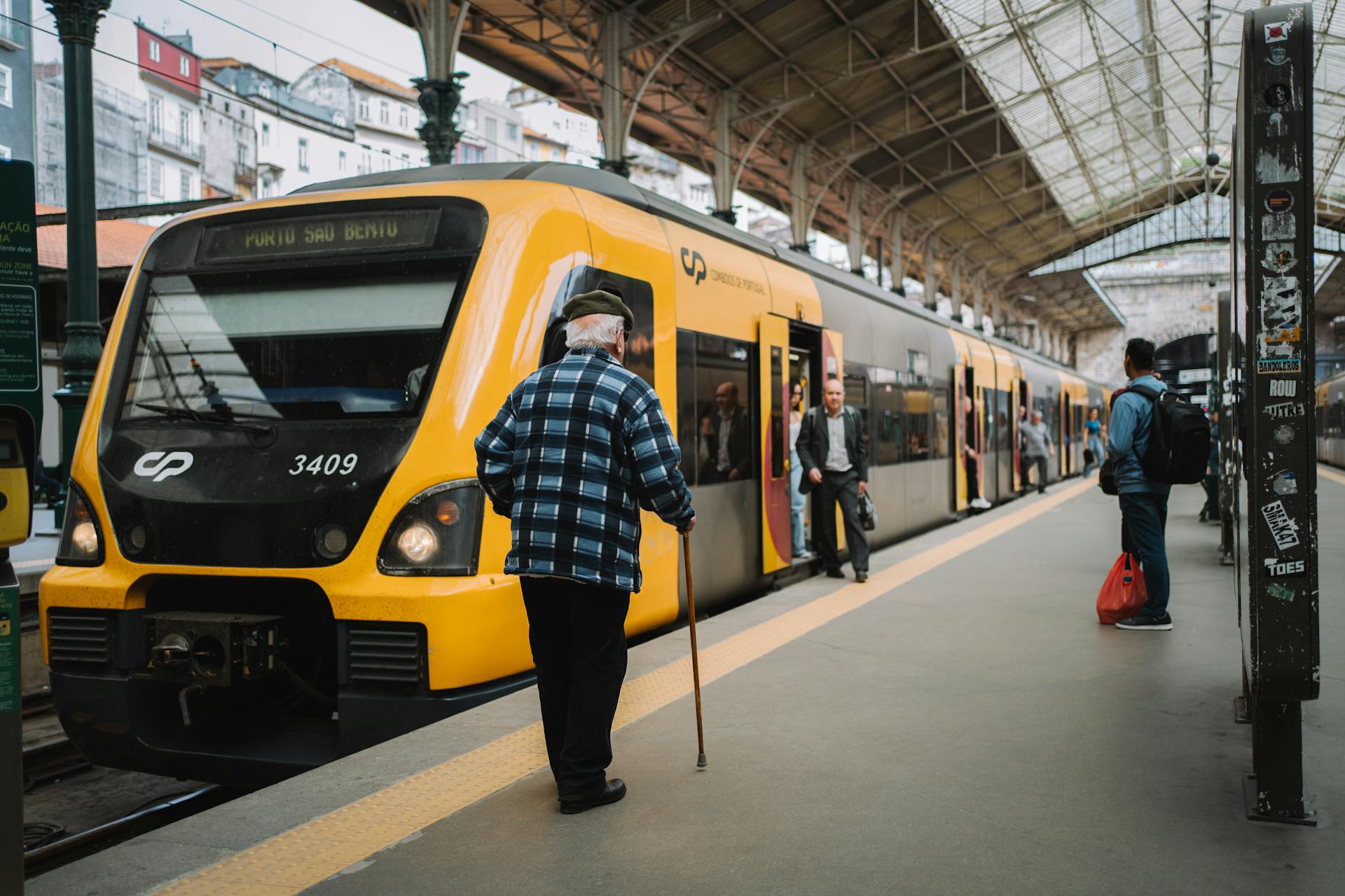 A senior man with a walking stick standing by a yellow train at Porto São Bento station.