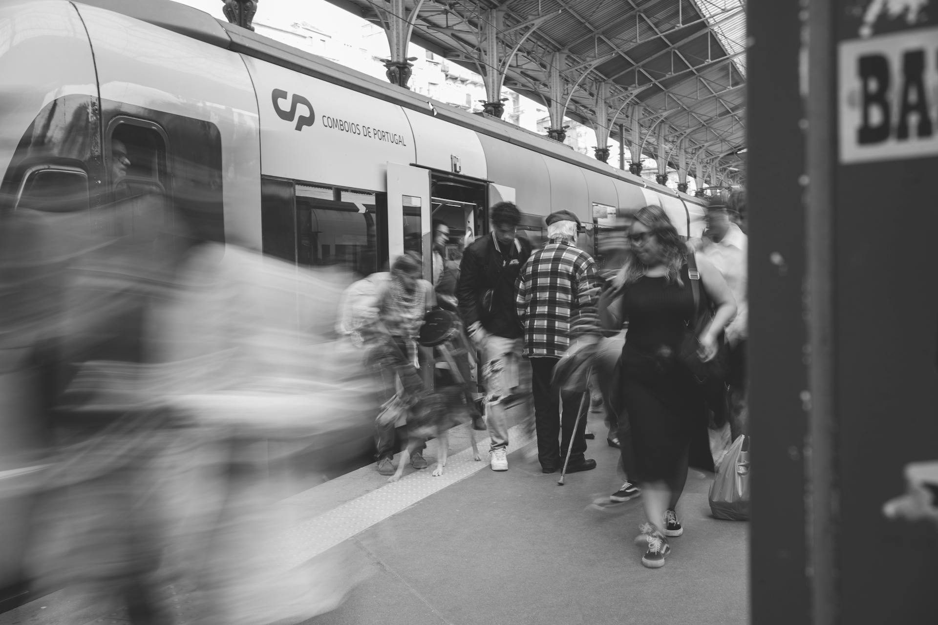 A black and white scene of commuters at a Lisbon train station, showcasing urban movement.