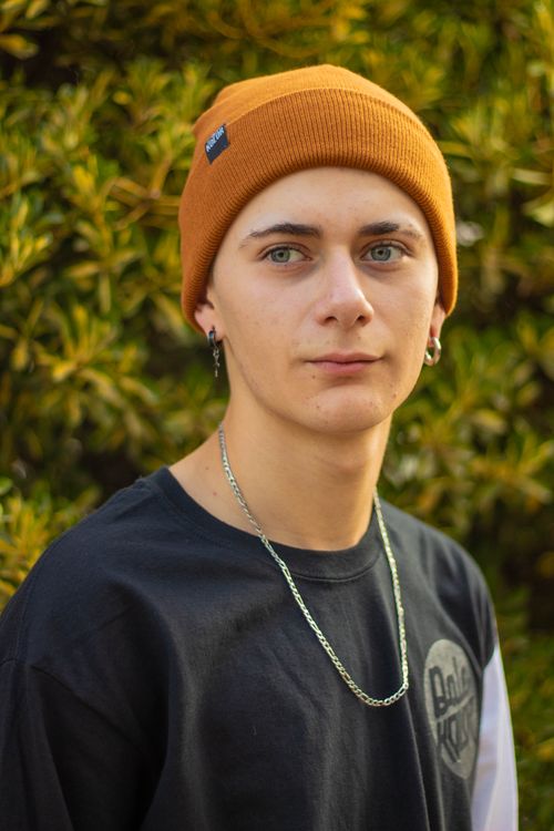 Free Stylish teenager in an orange beanie poses outdoors with a serene expression. Stock Photo