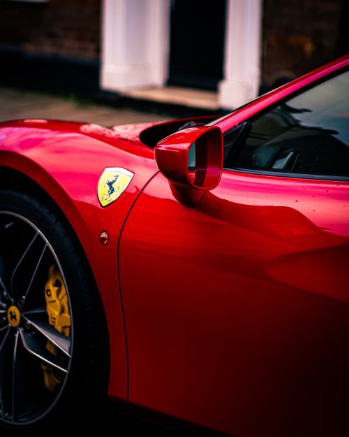 Free Close-up of a red Ferrari sports car showing side mirror and logo in an urban setting. Stock Photo
