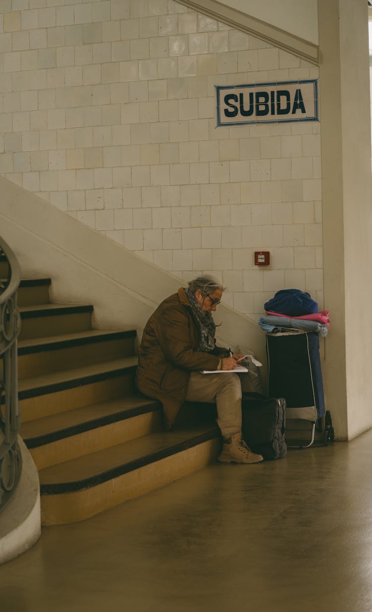 Elderly Person Sitting On Stairs And Writing