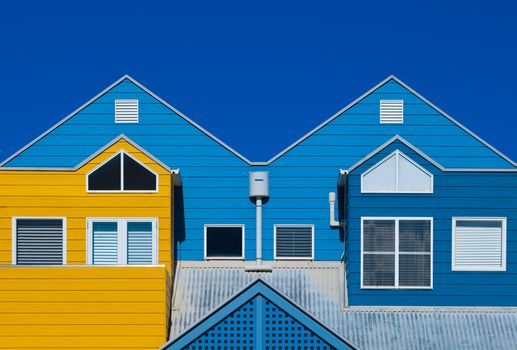 Bright blue and yellow facades of modern houses with symmetrical designs under a clear sky.