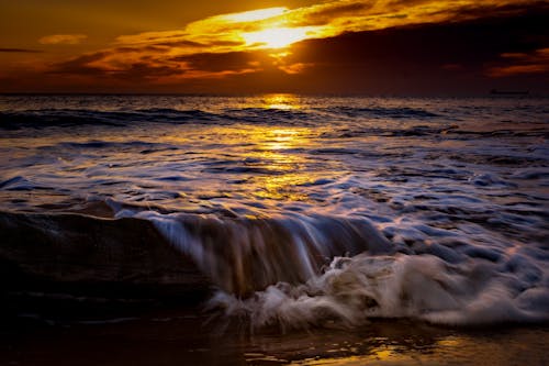 A sunset over the ocean with waves crashing on the shore