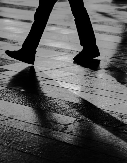 Free Shadowy silhouette of legs walking on a wet urban street reflecting rainy cityscape. Stock Photo