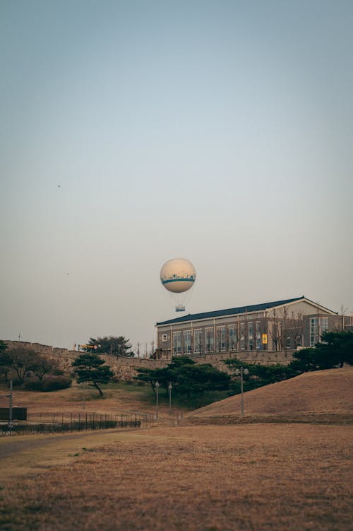 A hot air balloon flying over a field with a building in the background
