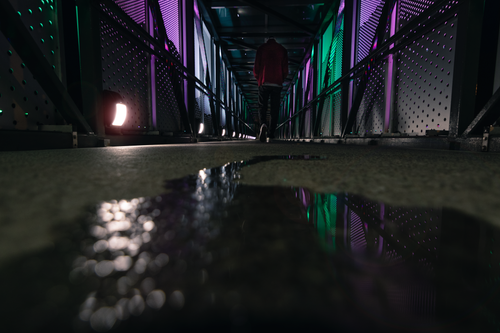 Free Low-angle view of a person walking through a colorfully lit tunnel in Knoxville at night, creating a reflective atmosphere. Stock Photo