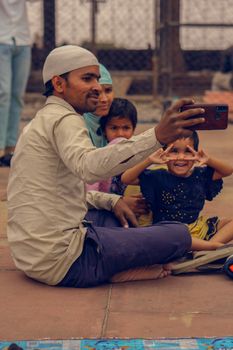A family of four joyfully takes a selfie together while seated outdoors.