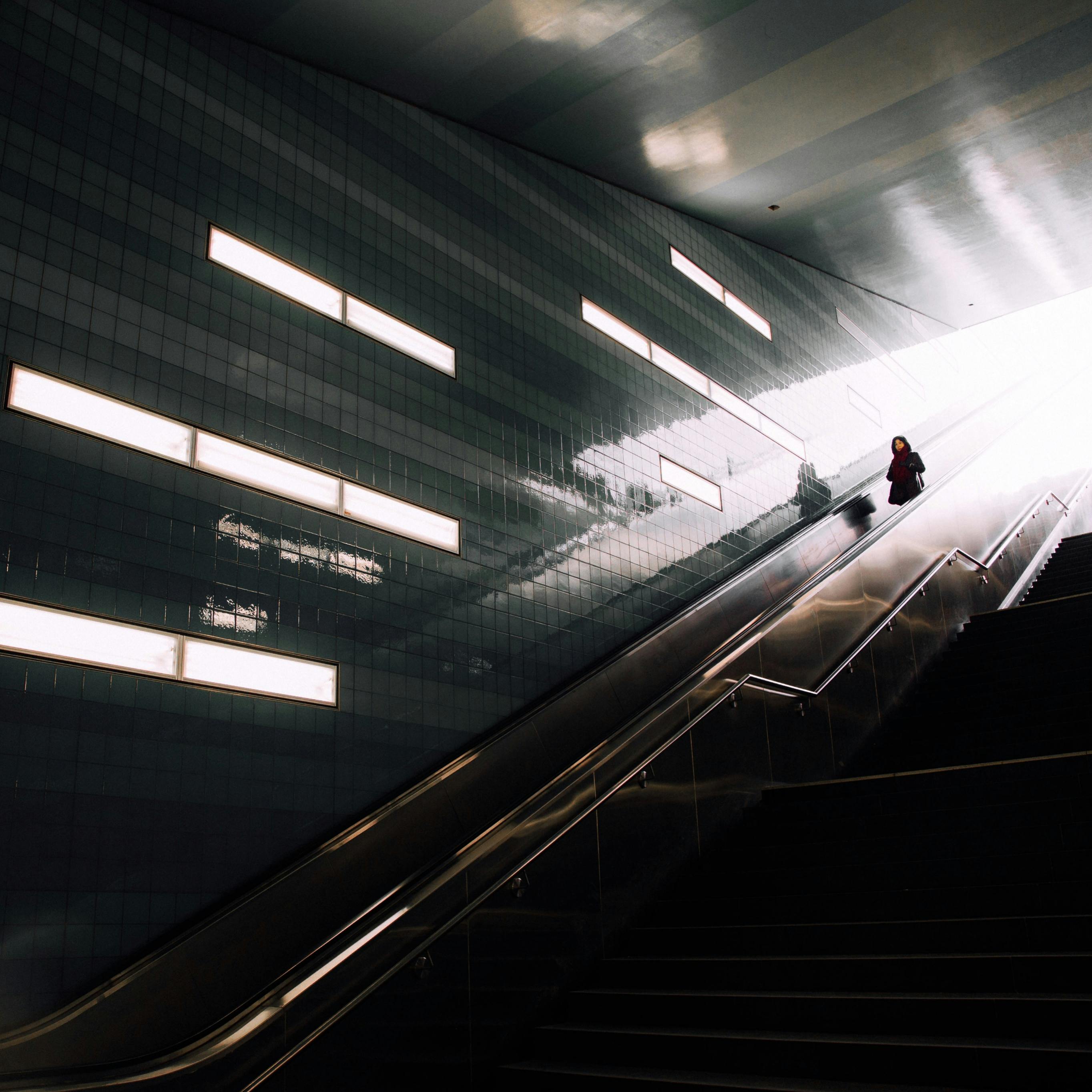 Dramatic lighting on a woman ascending an escalator at Überseequartier station, Hamburg.