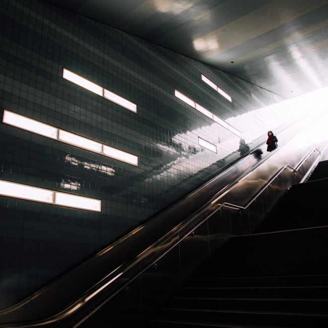 Dramatic lighting on a woman ascending an escalator at Überseequartier station, Hamburg.