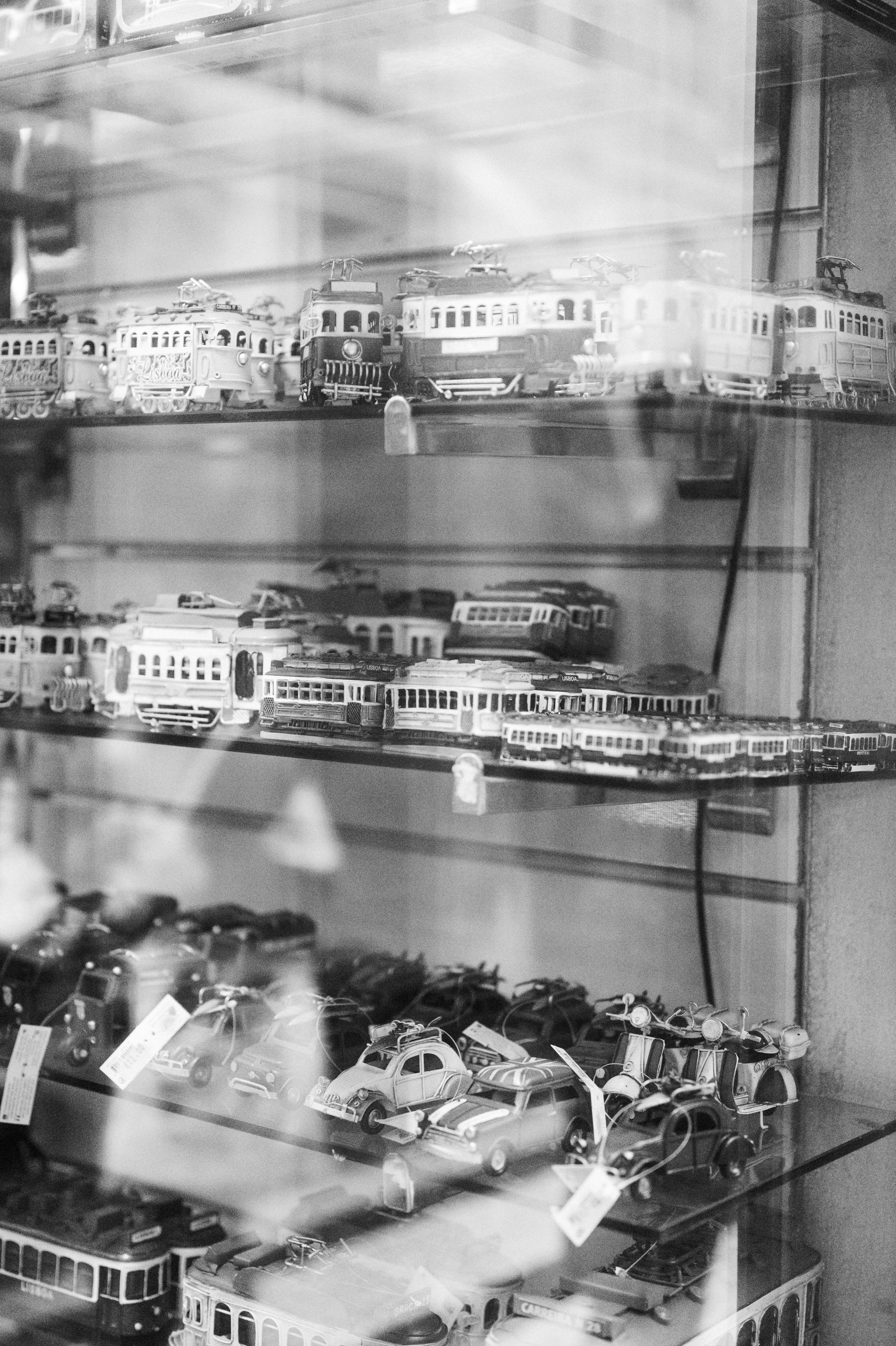 Black and white photo of vintage toy cars displayed on glass shelves, reflecting shop ambiance.