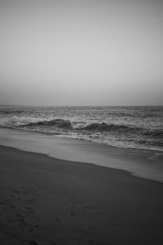 Peaceful black and white image of waves crashing on a sandy beach at dusk.
