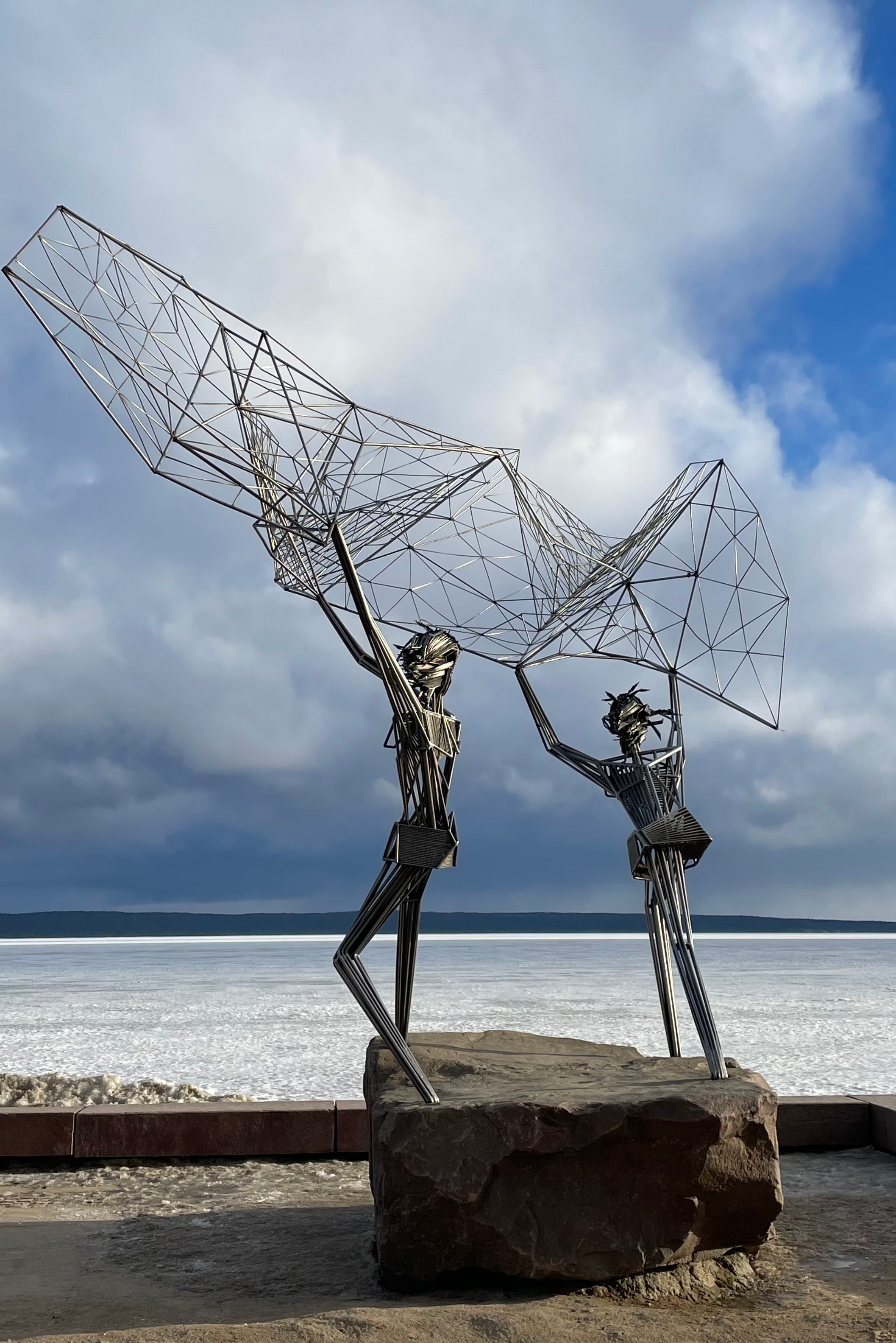 Metal sculpture of fishermen with a net by Lake Onega in Petrozavodsk, Russia, under a cloudy sky.