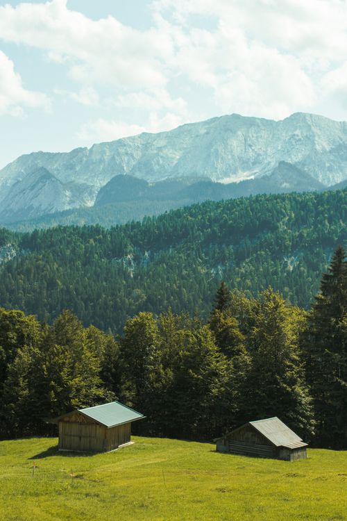 Free Beautiful view of rustic cabins on a green hillside with majestic mountains in Garmisch-Partenkirchen, Germany. Stock Photo