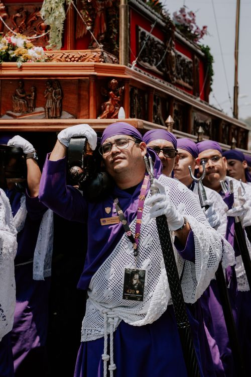 Free Men in purple robes participate in a Holy Week procession, carrying a religious float through city streets. Stock Photo