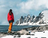冬天，一名身穿红色夹克的女子在海边的雪山中徒步旅行