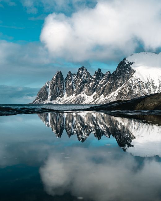 Breathtaking view of snow-capped mountains reflecting in a still lake under a clear, blue sky.