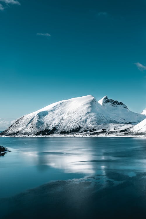 Gunung Yang Tertutup Salju Dekat Perairan Tenang Di Bawah Langit Biru Yang Jernih