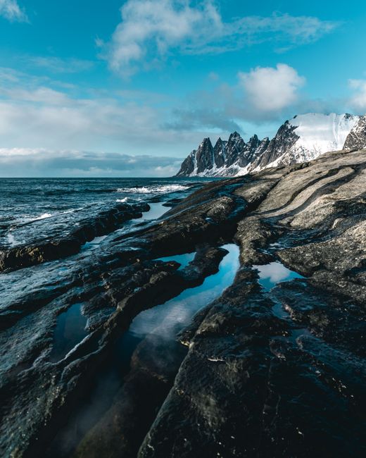Majestic view of snow-capped mountains and rocky seashore under a vibrant sky in winter.