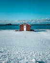 迷人的孤立海滩小屋位于白雪皑皑的海岸上，拥有平静的海洋背景和清澈的冬季天空
