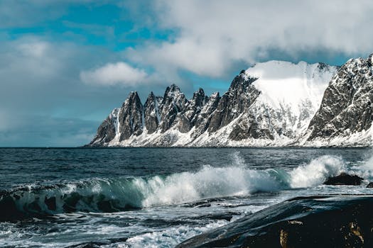 冬日海景令人惊叹，白雪皑皑的山脉与汹涌的海浪在多云天空下交相辉映