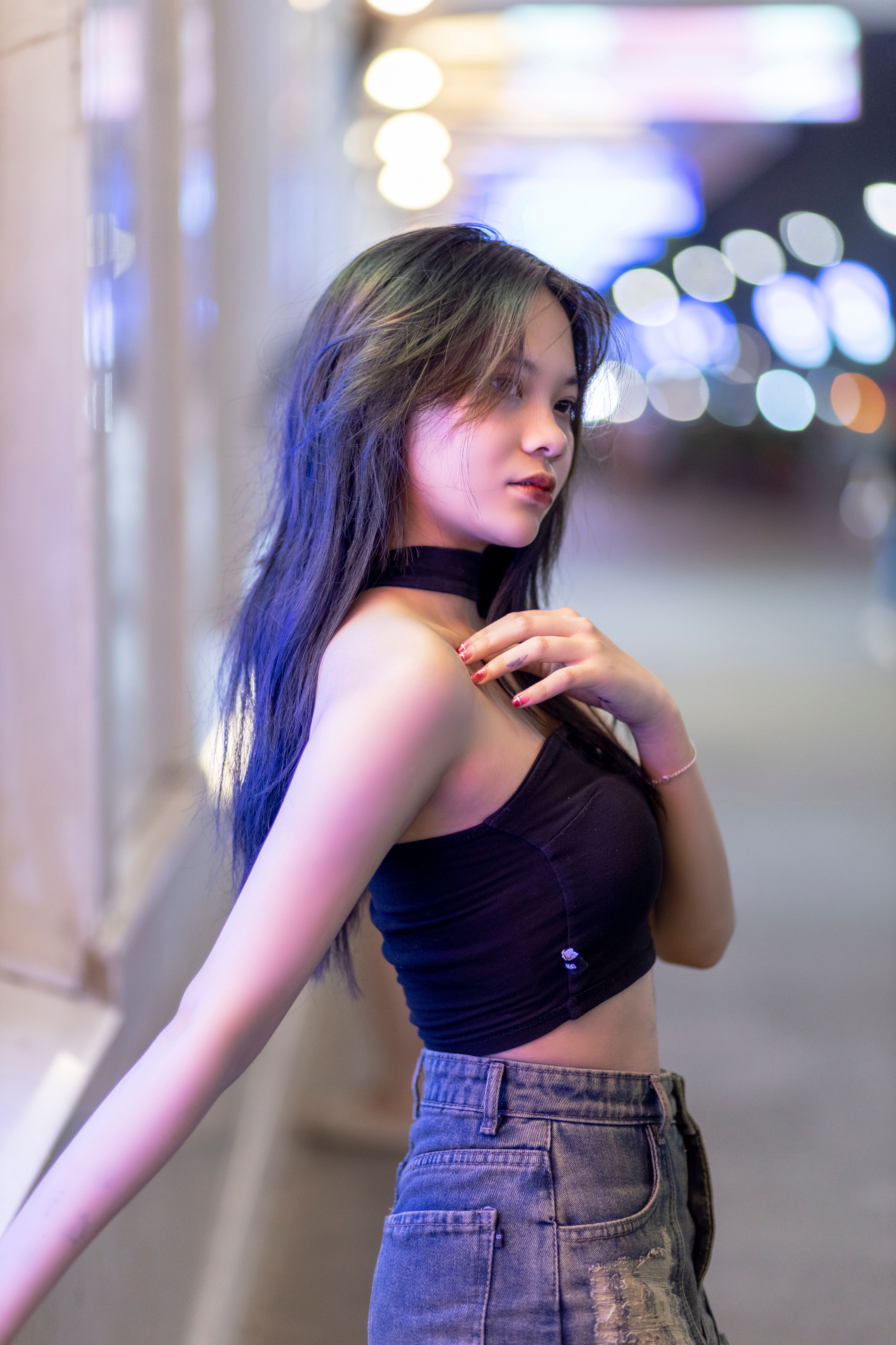 Chic portrait of a young woman in black top and jeans against blurred city lights.