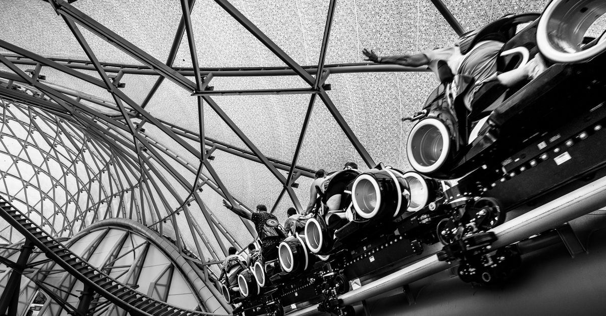 Black and white image of a roller coaster ride under a glass roof structure, capturing the excitemen