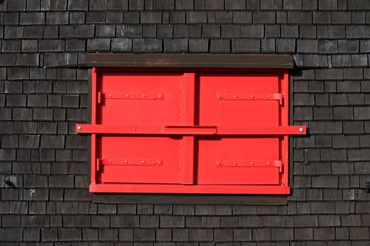 Red window shutters on a rustic dark wood wall, highlighting architectural contrast.