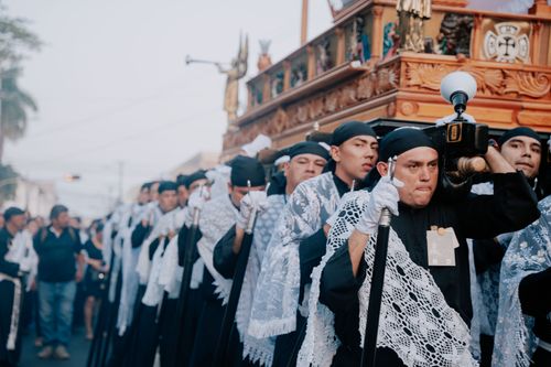 Free Men in traditional garments carry a ceremonial altar in a religious procession, drawing a diverse crowd in an urban setting. Stock Photo