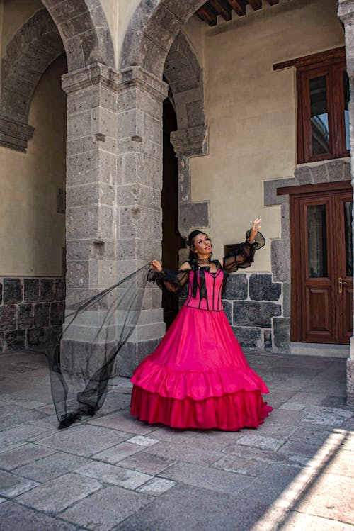 A woman in a pink dress is posing in front of a building