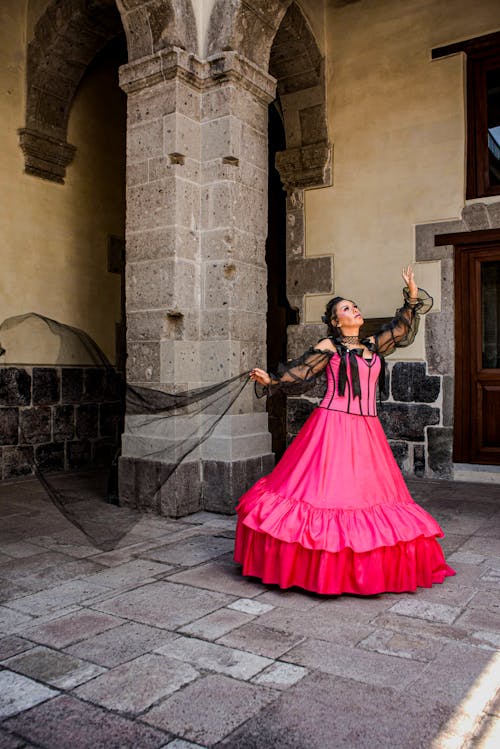 A woman in a pink dress is dancing in front of a stone building