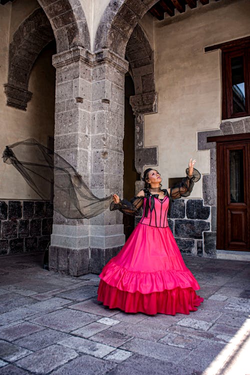 Free A woman in a pink dress is standing in front of a stone building Stock Photo