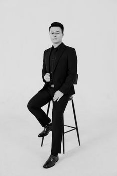 Black and white portrait of a fashionable man sitting in a studio, exuding elegance.