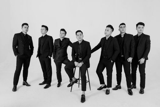 Elegant black and white studio portrait of seven men in stylish suits, showcasing formal fashion.