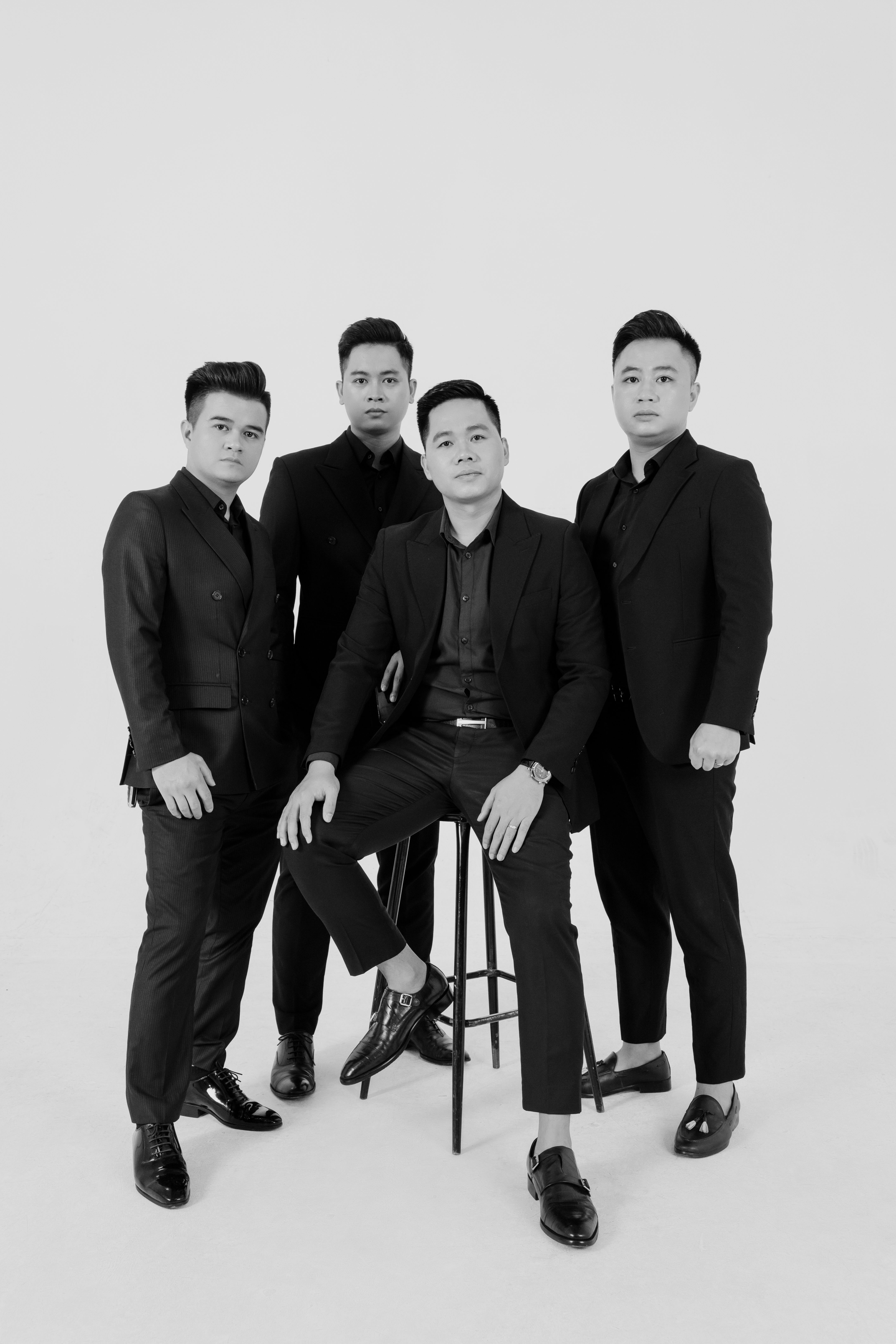 Four men in suits posing for a stylish black and white studio portrait.