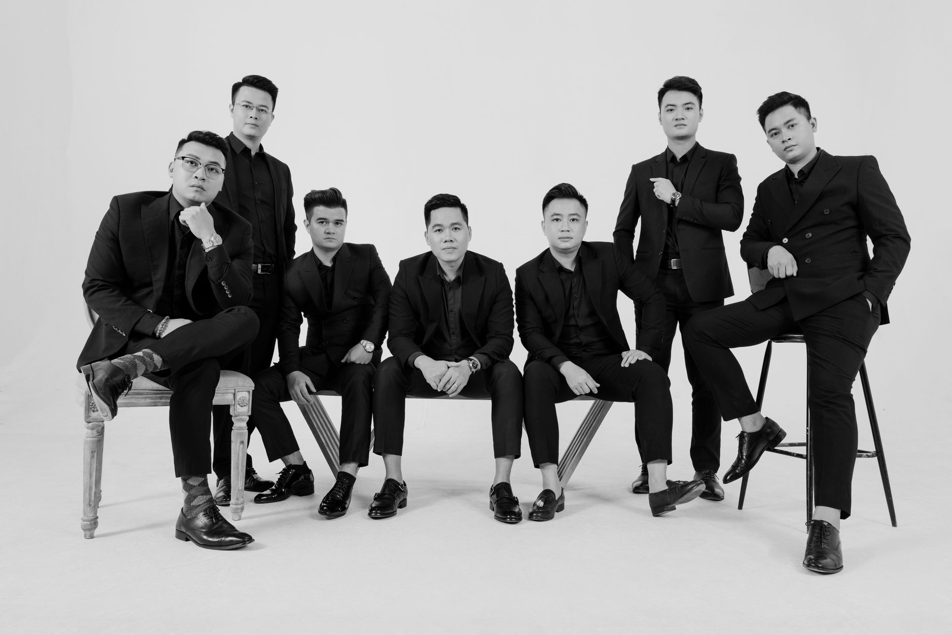 Stylish group of men in black and white suits posing in a studio. Elegant and professional.