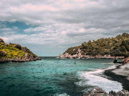 A beach with rocks and water under a cloudy sky